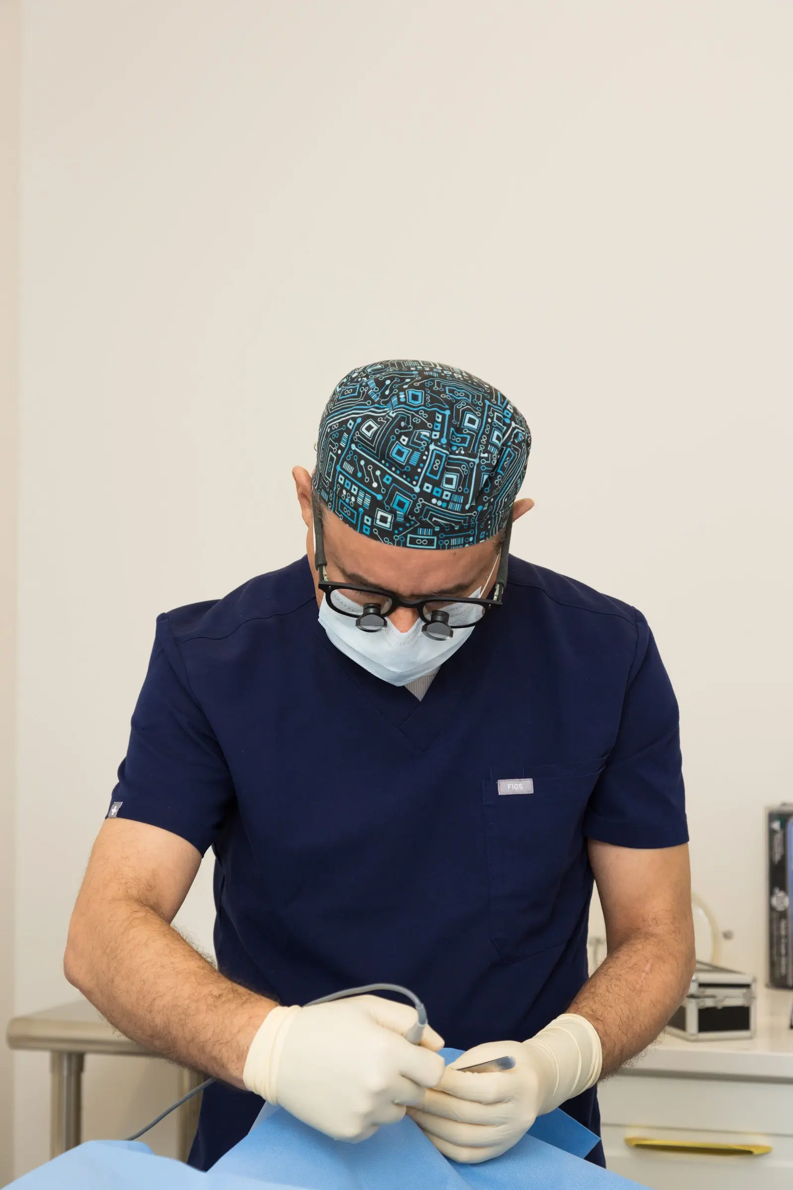 Dr. Kamal Tumi in surgical scrubs, cap, mask and gloves